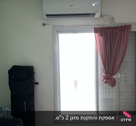 מזגן מותקן על קיר מעל חלון עם וילון ורוד